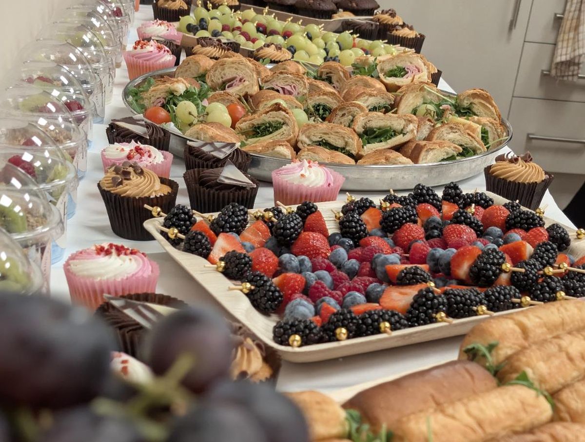 A breakfast buffet table with yoghurt pots, berry skewers, croissant rolls and cupcakes
