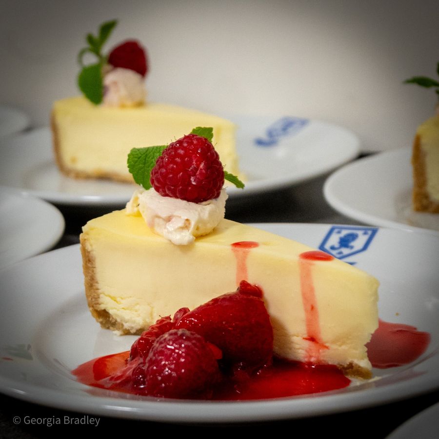 A slice of cheesecake with raspberry sauce, fresh raspberries and mint
