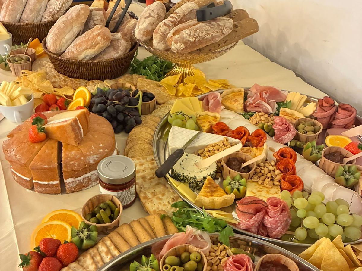 A party buffet table with grazing platters, bread baskets, crackers, fruit and cakes